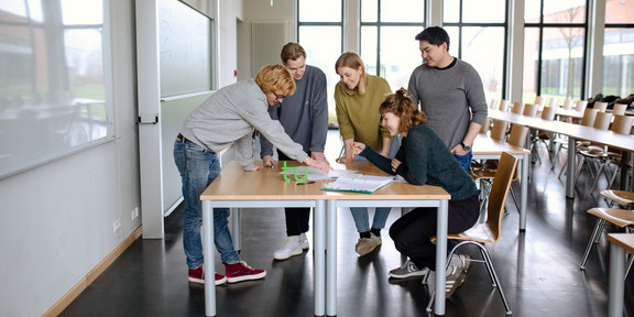 Five students stand around a table.