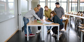 Students group work_04 Five students stand around a table.