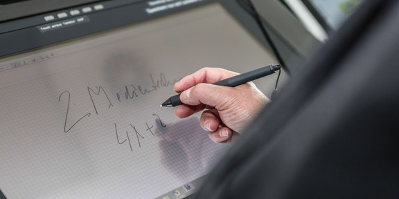 Writing at the lecture hall desk Screen of a lecture hall desk where someone is writing with a pen in hand.