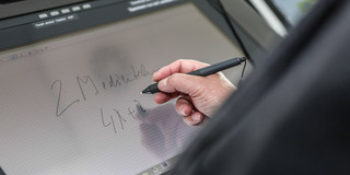 Am Hörsaalpult schreibend Bildschirm eines Hörsaalpults, an dem jemand mit einem Stift in der Hand schreibt.